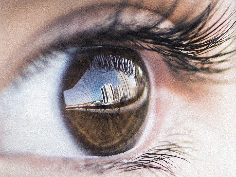 Close up image a human eye with long eyelashes and a brown irsis that refelcts a cityscape.